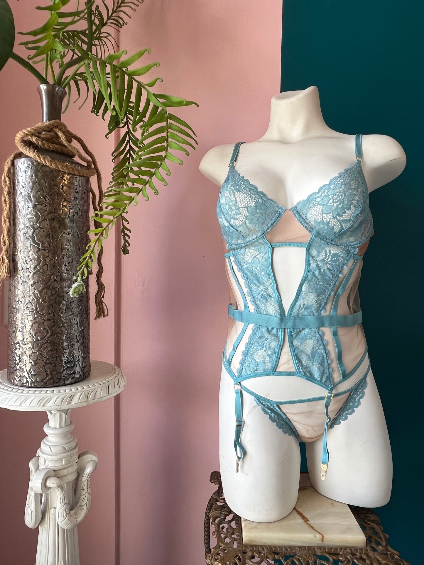 Mannequin wearing a blue lace lingerie set with a decorative plant and vase in the background.