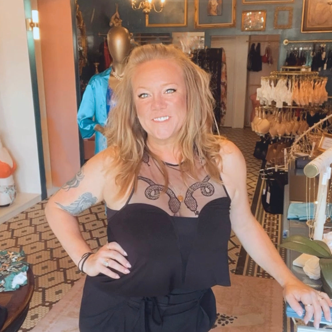 Woman in a black outfit standing in a store with mannequins and products in the background.